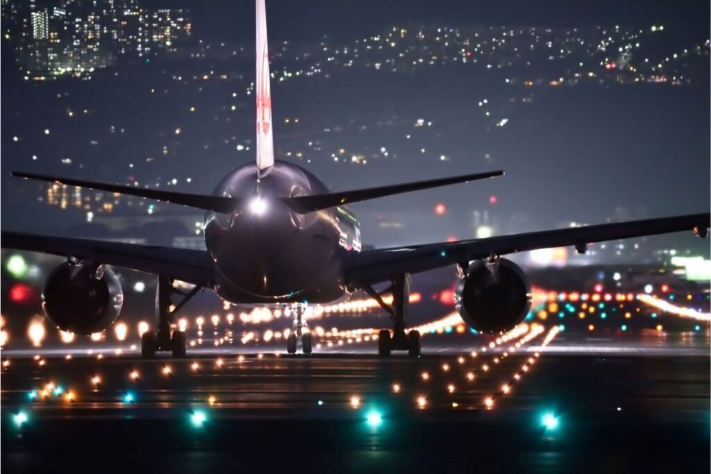 A jet plane landing at night-time on a lit up runway.